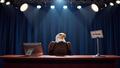 Empty late-night desk under stage lights, a blinking On Pause sign, and a worried bald eagle perched on a teleprompter.