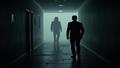 A lone gamer is shadowed by a looming stalker silhouette trailing through a dim hallway.