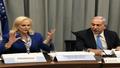 Netanyahu and Cindy McCain at a long table, microphones bristling, both gesturing at a dictionary while aides swap bottled water with media lanyards.