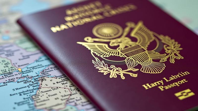 Close-up of a passport stamped excessively, with a chocolate box beside it labeled ‘Assorted National Crises.’
