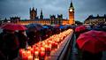 Candles and umbrellas near Westminster as thousands stand in rain, placards balanced against wind and memory.