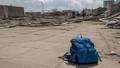 A child’s backpack amid broken concrete and sun-bleached aid tarps; a reporter’s notebook open to blank, stunned lines.
