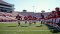 A ranked football team runs onto a field flanked by empty bleachers, ushers high-fiving over the echo.