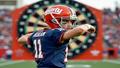 Jaxson Dart in a Giants helmet, poised mid-throw, with a massive dartboard disguised as a playbook behind him.
