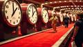 Red carpet shaped like a conveyor belt, celebrities riding it past giant clocks while interns hurl branded popcorn, as a judge’s gavel smacks a clapperboard.