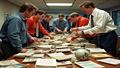 Front office staff sifting through a pile of discarded playbooks and helmets labeled 'waiver wire,' as a coach triumphantly holds a faded 'slightly used slot corner' tag.