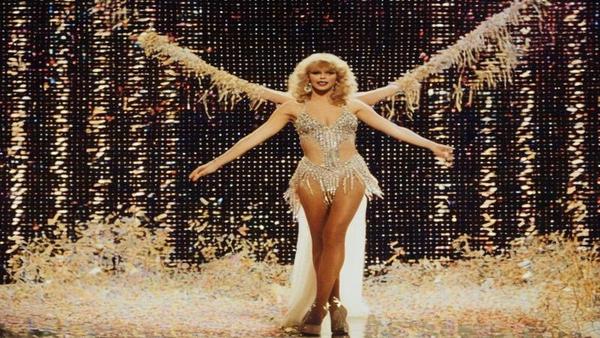 Taylor in rhinestone showgirl regalia, bestriding a calculator-shaped stage; confetti forms the number 15.