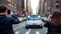 A Waymo self-driving taxi glides down a busy Manhattan street while bystanders photograph the moment with their phones.