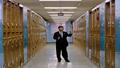 Xi at a gilded podium, wagging a finger; backdrop shows pastel world map and a school hallway of lockers labeled 'Tariffs.'