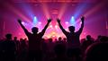 Two illuminated silhouettes hover over a crowd of excited fans in neon glow.