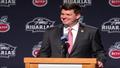 Ryan Day at a podium, mid-gesture, grinning like a man who just discovered defense counts as offense.