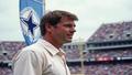 Troy Aikman on the sideline, eyes like a laser, as a Cowboys banner flaps behind him.