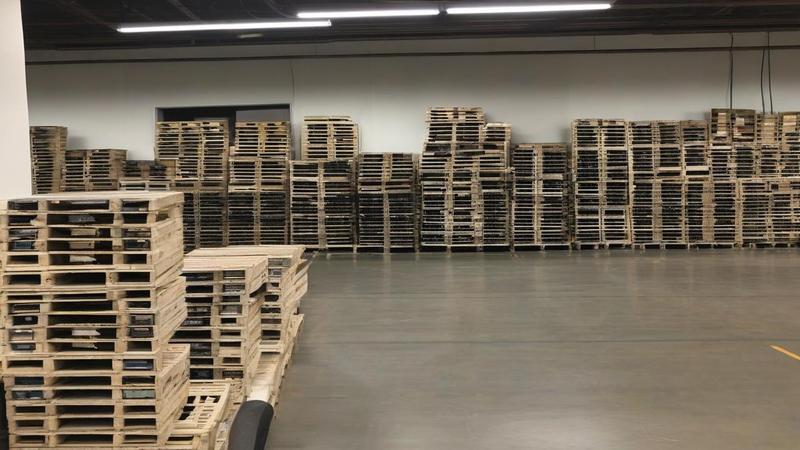 Pallets of semiconductor boxes labeled 'not dumping' teeter beside a spreadsheet projected like a cathedral window, accountants praying for margins.