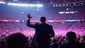 Will Smith on stage, waving to a glitchy, repeating crowd loop, some faces identical, stadium lights too perfect, vibe uncanny.
