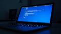 An office laptop displays a blue error screen as caffeine-fueled engineers whisper prayers to the reboot gods.
