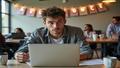 A harried intern stares at a laptop while a banner reads 'All at Once,' in a break room cluttered with coffee mugs.