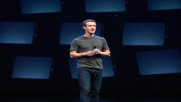 Mark Zuckerberg on a dark stage, haloed by screens, holding a sleek headset like a newborn business model.
