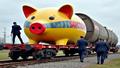 EU officials push a giant piggy bank labeled Sanctions onto a railcar marked Kyiv, while lawyers chase it with clipboards.