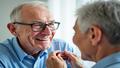 Close-up of an older adult smiling while a clinician fits a tiny hearing aid in a bright clinic.