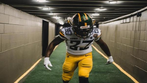 Brian Burns in stadium tunnel, helmet in hand, mid-step, frustrated after loss, fluorescent lights, security nearby.