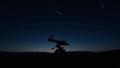 A lone telescope silhouettes against a velvet-black sky, a single Perseid comet threading the void.