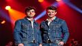 Noel and Liam take the stage in matching denim, eyes narrowed, nostalgia blazing in retro lighting.