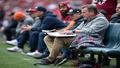 Coach slumped on sideline bench with playbook and blanket, mid-lie-down.