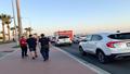 First responders and civilians take cover along Eilat’s waterfront as sirens wail, palm trees lean, and a clear sky pretends it had no idea.