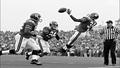 Giants defensive back and Commanders receiver airborne for a pass, ball untouched, referee pondering Euclid, crowd caught between cheer and yawn under gray skies.