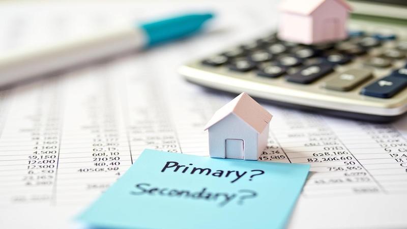 Close-up of dense financial footnotes with a highlighter, sticky notes reading ‘primary?’ ‘secondary?’ and a tiny house-shaped paperweight balancing on a calculator.