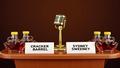 A podium flanked by maple syrup bottles and a gold microphone, as cue cards read 'CRACKER BARREL' and 'SYDNEY SWEENEY' like quarterly earnings slides.
