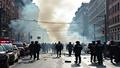 Smoke-laden street scene with police securing a chaotic aftermath and emergency responders at work.