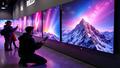 Shoppers kneel before a wall of luminous LG OLEDs, price tags shimmering like distant galaxies, as a heroic remote control rests atop a mountain of bubble wrap.